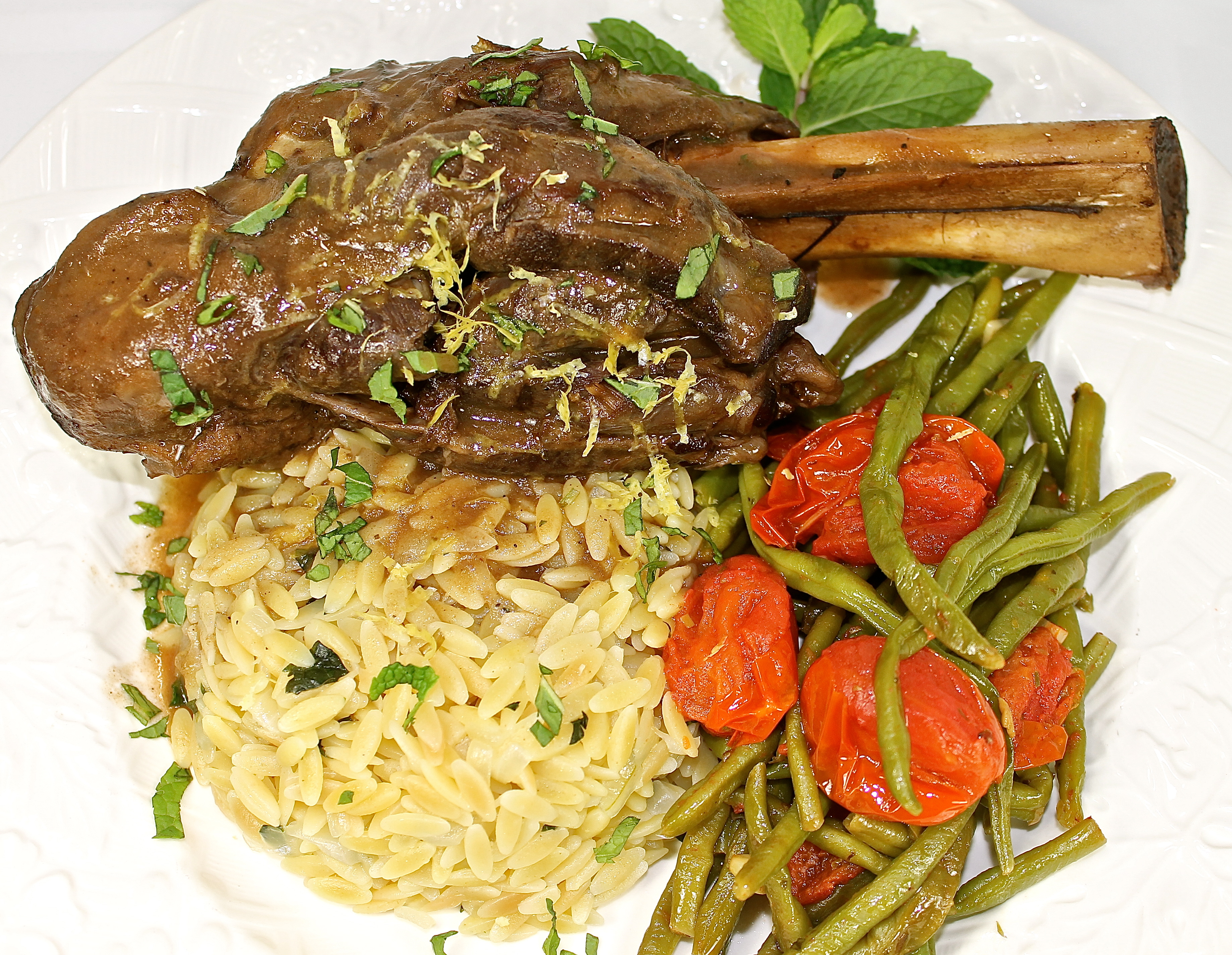 Slow Braised Lamb Shanks Served With Lemon Orzo, Green Beans And Tomatoes 