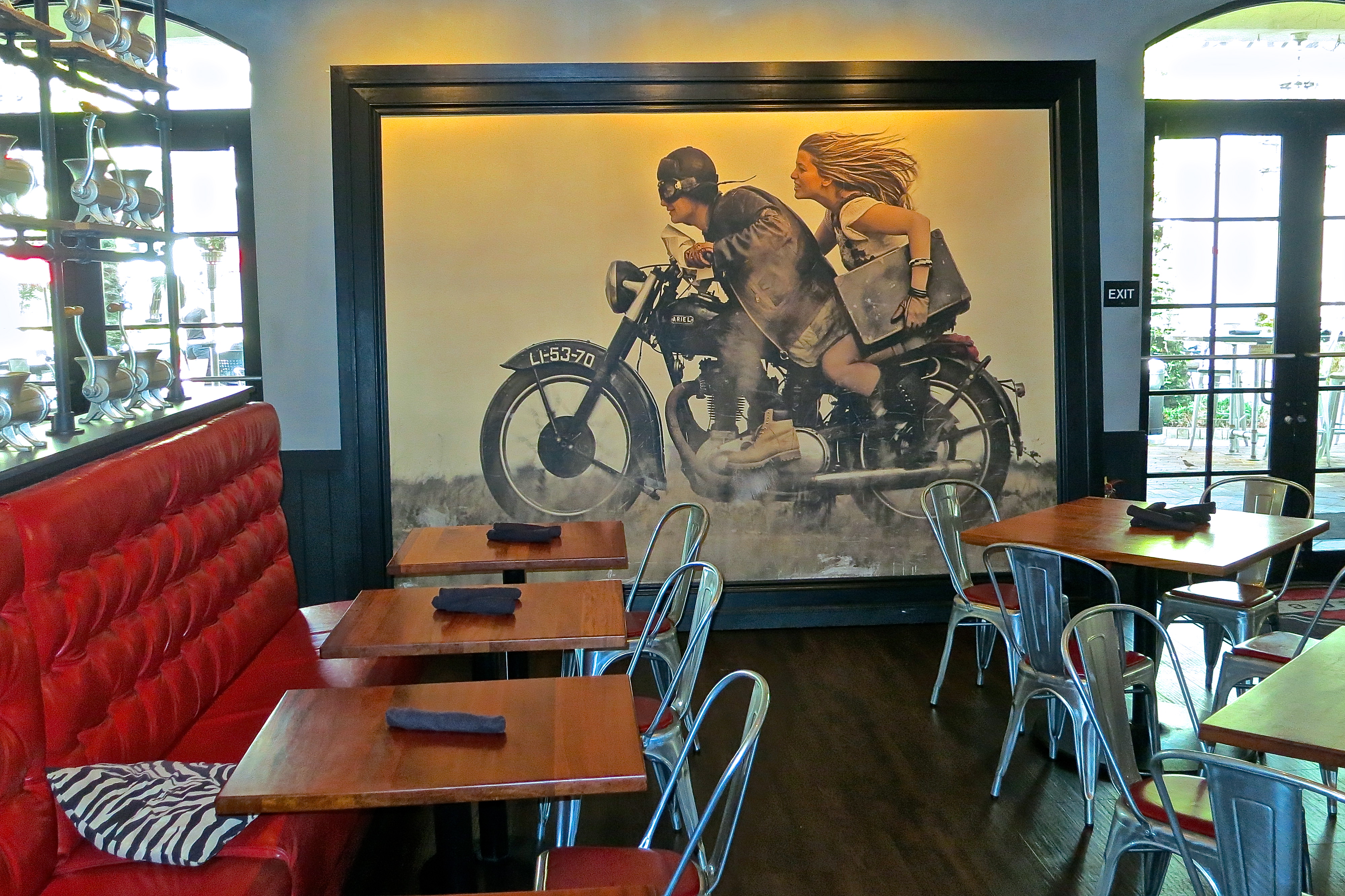 A Large Retro Picture Of A Man And Woman On An Antique Motorcycle Leans Against One Wall Of The Burger Bar