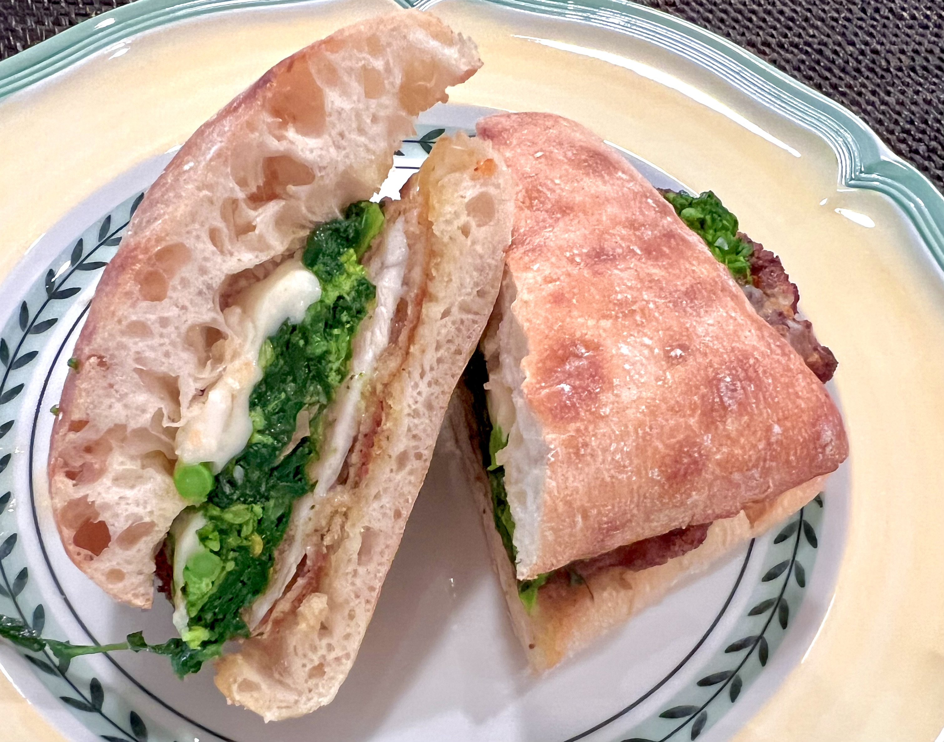 A cross-section cut of a deli-style chicken and broccoli rabe sub, highlighting the layers of crunchy chicken, garlicky greens, and gooey melted cheese